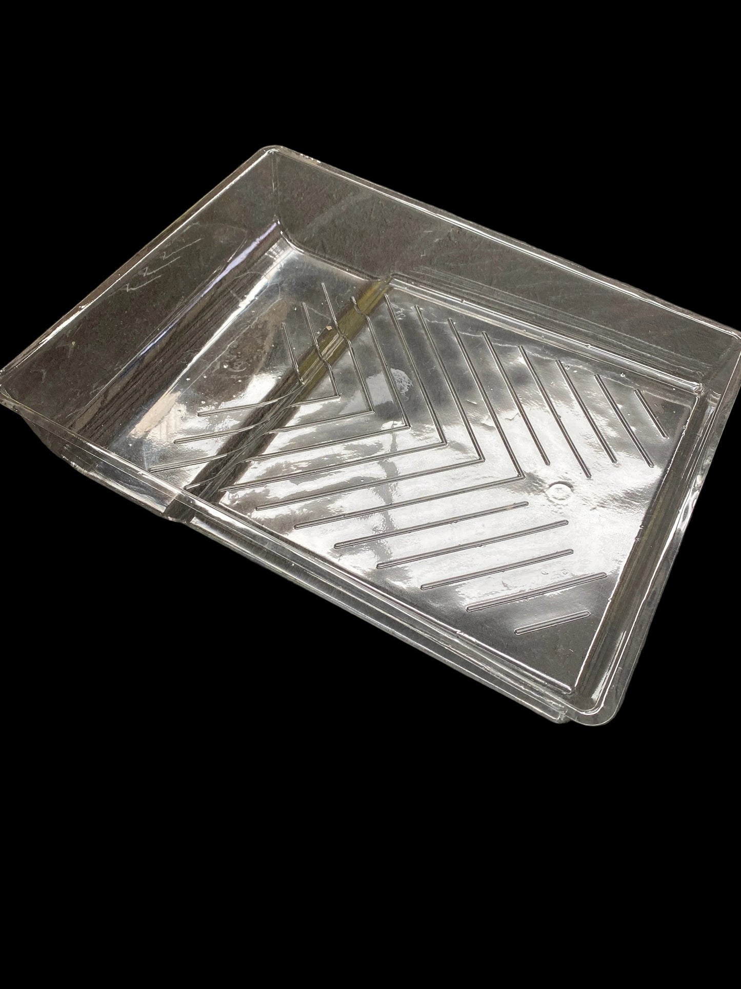 A clear plastic rectangular tray with a ribbed bottom, shown from an overhead angle on a dark textured surface.