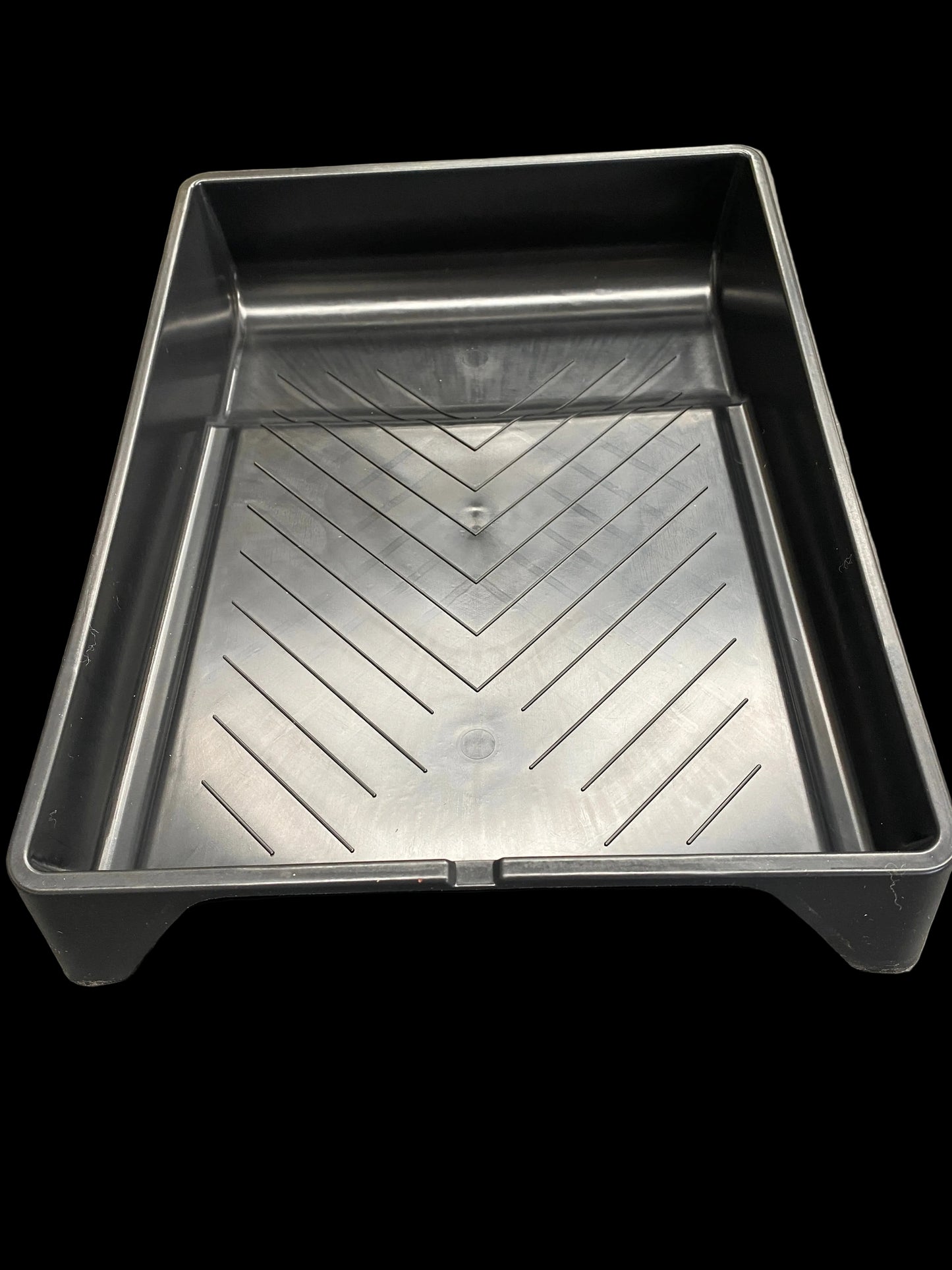 A rectangular black plastic paint tray with a textured, ribbed bottom surface, photographed from an angled overhead perspective on a gray textured background.